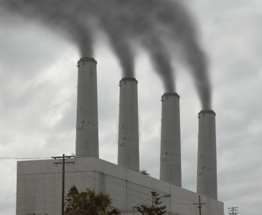 An image of four large stack exhausts connected to a building with smoke plume s coming out the top.